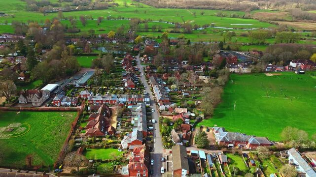aerial drone landscape shot over Romsey, Hampshire, England Town village in spring sunset surrounded by nature trees and fields with golden warm light above. Calm quiet roads and paths below