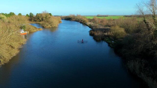 Aerial view of a four person rowing shell and its crew in action on the River Great Ouse in Ely Cambridgeshire during a tranquil golden hour sunset with reflections on the calm water