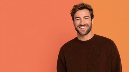 Obraz premium Cheerful young man grinning at camera wearing cozy brown sweater over vibrant orange and coral background with copy space for professional corporate branding