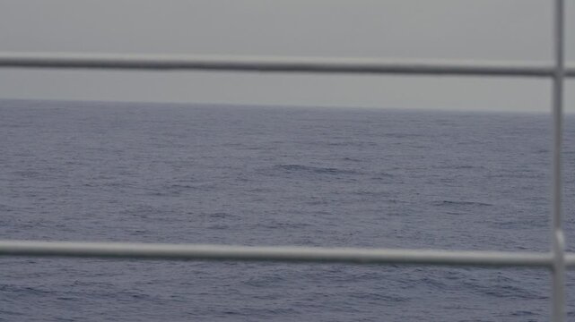 Contemplative view of slow dark blue Antarctic ocean swells through ship railing bars under flat grey overcast sky while crossing Drake Passage