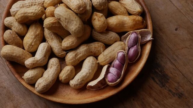 Boiled peanuts in shell with purple violet skin kernels revealed on wooden plate on rustic wood table, healthy traditional Asian snack nutrition closeup