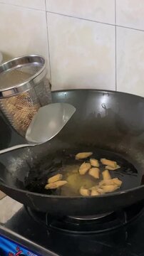 Freshly fried crispy popiah rolls being lifted from hot oil with a metal strainer. Golden crunchy traditional CNY snack drained for festive celebration.