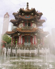 Fototapeta premium Description: Ornate traditional Chinese temple pavilion with intricate roof details and symmetrical stone stairways, surrounded by greenery under an overcast sky
