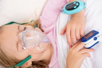 Naklejka premium Young person, girl receiving oxygen therapy, Child lies with oxygen mask and pulse oximeter on finger, patient health tracker, pediatric respiratory care, recovery hospitalization, health monitoring