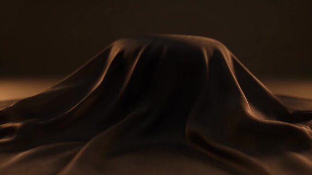 A dark brown fabric mound sits on a white surface with a warm glow in the background