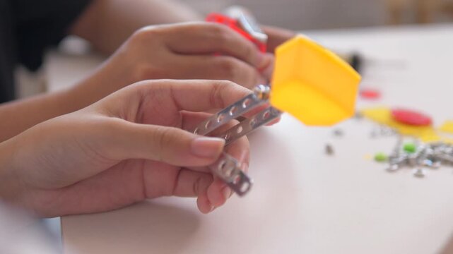 Close up of child hands assembling 3D printed robot model on table. Concept of STEM education, robotics learning, creativity, and technology development