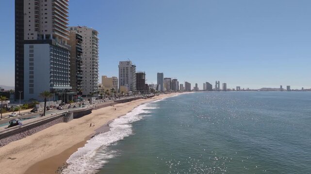 Vista aerea de paisaje urbano en la costa del pacifico en un dia soleado, mostrando olas calmadas y eduficios  en horizonte