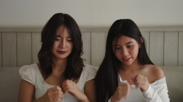 Young Asian mother and daughter perform a simultaneous choreography happy and smiling sitting on a comfortable sofa