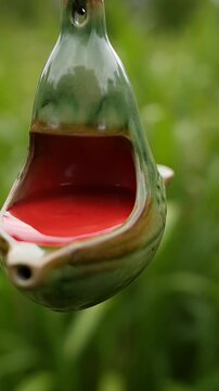 Ceramic bird feeder, shaped like a stylized bird, with a red interior, hangs outdoors