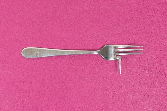 Closeup of a broken and bent silver cutlery fork, The bent fork illustrates the concept of inefficiency, harm, danger, useless products and enshitification.