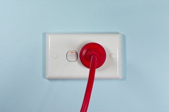 Closeup of a red Australian electricity cord plugged into a power socket outlet. This electrical power cable illustrates the concept of expensive energy and bill cost savings.