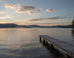 Fototapeta premium A tranquil wooden dock extends into a calm body of water at sunset, reflecting warm golden hues and surrounded by hills in the distance.