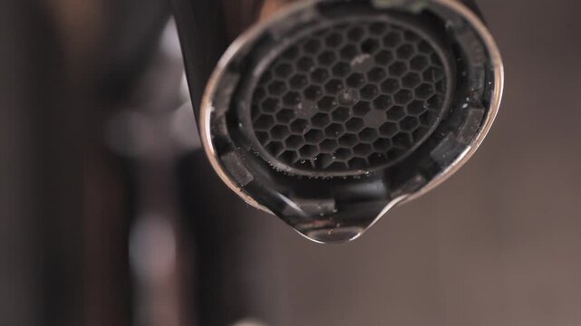 Extreme close up of a water droplets falling from a chrome faucet aerator with honeycomb mesh pattern in a bathroom