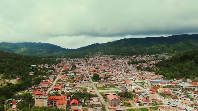 Aerial drone view moving forward and slowly descending toward the distant city of Villa Rica, Chanchamayo, Peru, showing green mountains and a cloudy sky in the high jungle.