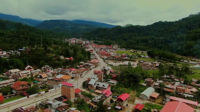 Close aerial drone orbit over the city of Villa Rica in Chanchamayo, Peru, showing residential rooftops and streets surrounded by misty high jungle and green mountains.