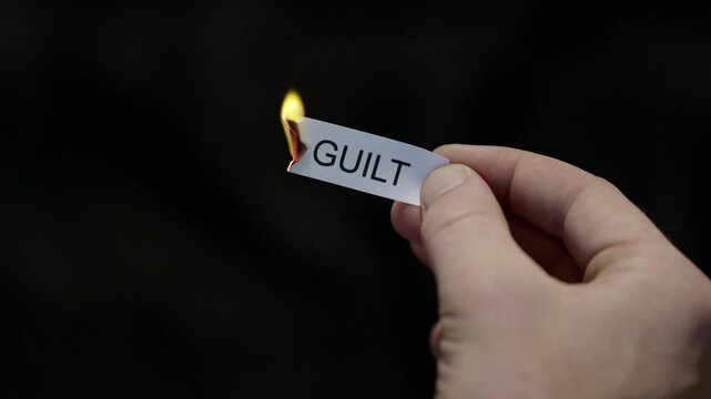 Burning Away Guilt - Hand Setting Fire to Paper note Marked &ldquo;GUILT&rdquo;, Powerful Release of Criticism, Guilt and Shame, Dark Cinematic Close-Up. Mental health, therapy