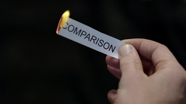 Burning Away Comparison - Hand Setting Fire to Paper note Marked &ldquo;COMPARISON&rdquo;, Powerful Release of Criticism, Guilt and Shame, Dark Cinematic Close-Up. Mental health, therapy