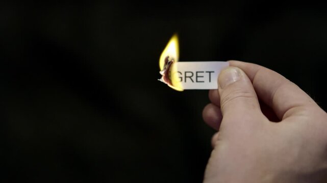 Burning Away Regret - Hand Setting Fire to Paper note Marked &ldquo;REGRET&rdquo;, Powerful Release of Criticism, Guilt and Shame, Dark Cinematic Close-Up. Mental health, therapy