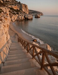 Fototapeta premium A serene coastal staircase leads down to a rocky beach at sunset, with warm golden hues reflecting off the calm sea.
