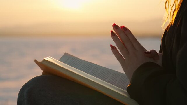 Close-up of a girl reading a book in the sun. The girl holds a Bible in her hands and studies the word of God in search of truth and spirituality.
