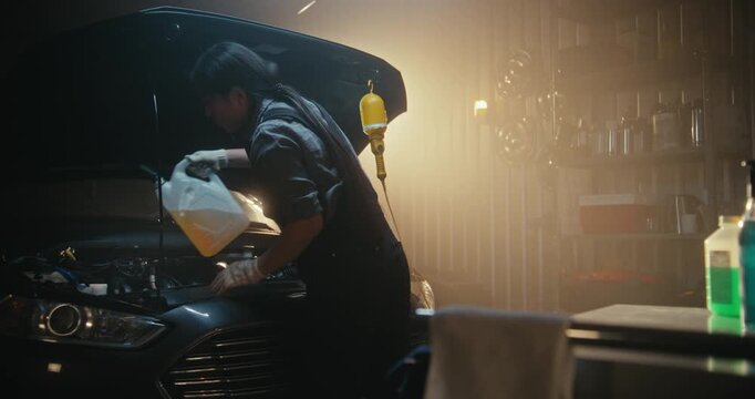 Concentrated Female Mechanic Adds Coolant to Engine Bay of Vehicle in Stylish, Well Equipped Garage. Concept Preventive Maintenance, Technical Skill, and Growing Role of Women in Automotive Industry.