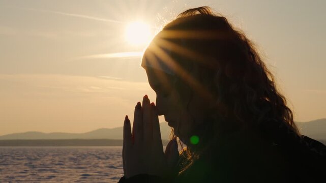 A lonely praying girl against the sunset background asks God for forgiveness and blessings for a happy life. The concept of aspiration, luck and inspiration.