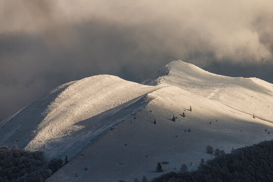 Breathtaking winter sunset over the snow-capped peaks of Polonina Carynska in Bieszczady Mountains. Dramatic golden light hitting the mountain ridge against dark moody storm clouds 