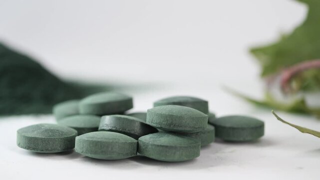 Close up view of green chlorella and spirulina powder and pills on a white background with a plant branch
