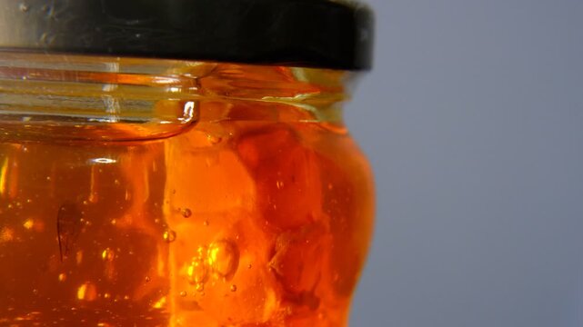 Golden Honey jam swirls gently in glass bottle product ,Close up super macro shot scene golden honey liquid bubbles in glass ,honey comb macro product studio shot with the bubble fluid texture
