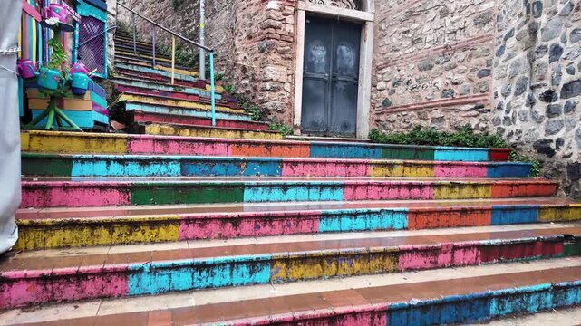 Low angle tracking shot of colorful painted stone stairs leading up narrow alleyway during rain in historic city