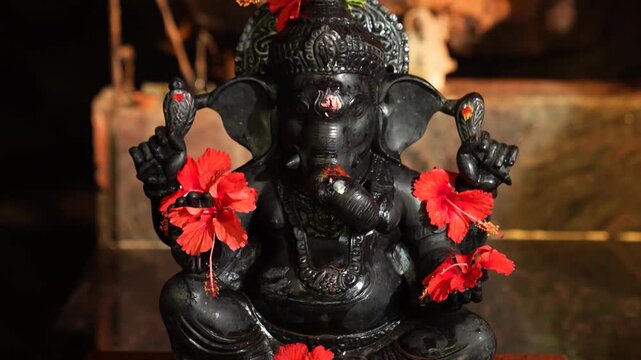 Black Lord Ganesha Idol Adorned with Hibiscus Flowers &ndash; Sacred Hindu Worship Scene.