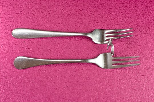 Two broken and bent silver cutlery forks entwined together like lovers. These forks illustrate the concept of romantic love, closeness, togetherness, companionship, desire, and lust.