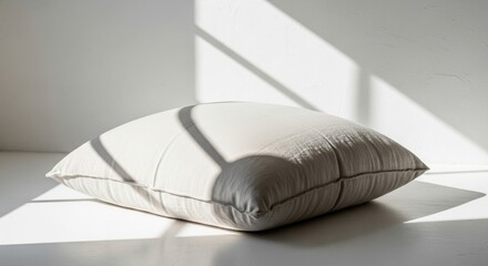 Obraz premium A textured, light-colored floor cushion rests peacefully in a sunlit room, casting soft shadows, perfect for creating a cozy relaxation space.