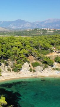 Aerial view of Alonaki Fanariou beach with clear turquoise water, pine forest, and distant mountains in Greece. Bright summer landscape ideal for travel and nature concepts.