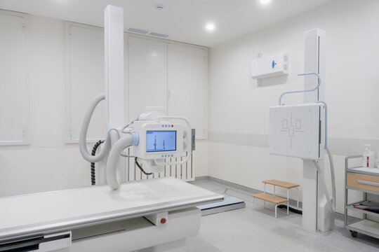 Bright radiology room with digital X ray equipment, detector panel and exam table in modern medical interior for diagnosis.