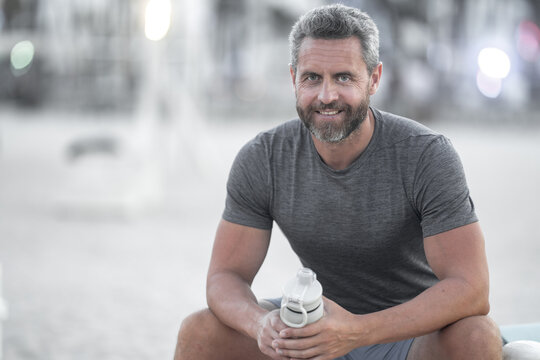 Sport fitness man resting on a bench outdoors. Mature fitness sport model sitting on a bench after a workout. Hispanic sports man taking a break after fitness. Fit guy resting after fitness.