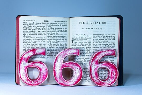 The number 666 with a bible open at the Book of Revelation in the holy Christian bible. A symbol of the number of the beast, King James version.