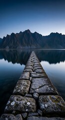 Fototapeta premium Stone pier leading into calm lake with mountain reflection at twilight