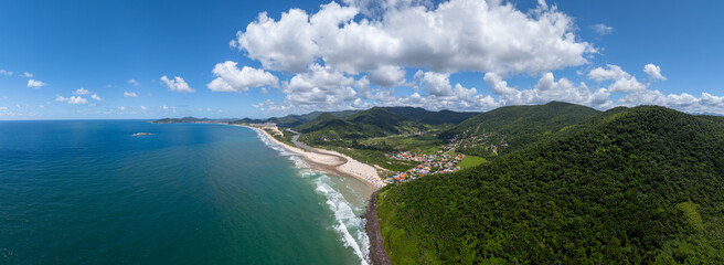Naklejka premium Aerial panorama of the tropical beach, little town and hidden in the green hilly terrain. Town of Siriu, Santa Catarina, Brazil