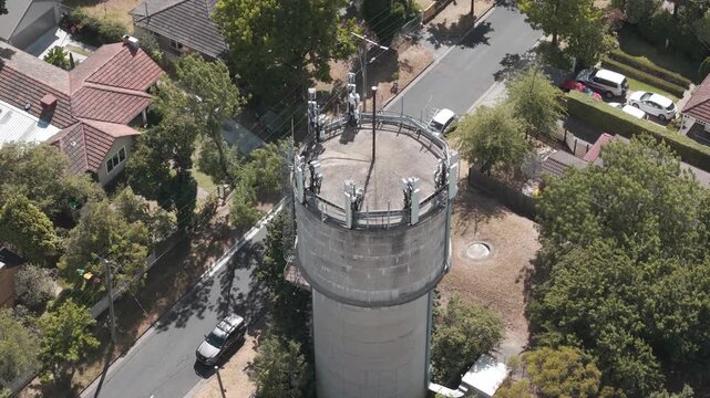 Drone footage captures Karen Reece Water Tower in a sunlit Melbourne suburb. Surrounded by houses, the concrete structure epitomizes suburban architecture from above.