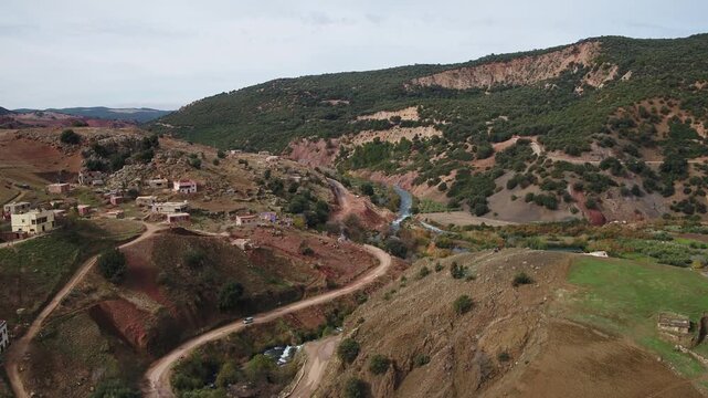 Drone aerial of a rural valley landscape with winding river, scattered houses, and mountain roads in the Middle Atlas near the Oum Er-Rbia basin.
