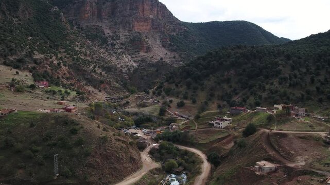 Drone aerial of a winding river valley with rural houses and mountain roads near the Oum Er-Rbia springs in the Middle Atlas Mountains of Morocco.