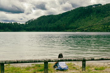 Fototapeta premium Woman Sitting Lakeside Near Forested Mountain