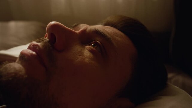 Close up of adult man with beard covering face with hands in despair lying on bed while going through emotional breakdown