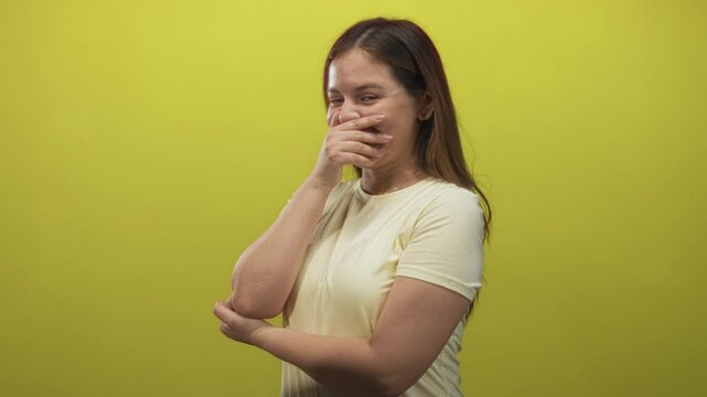Young caucasian woman covering mouth with hand in studio with lime backdrop and crossed forearm pose, slight smile; amusement reaction.