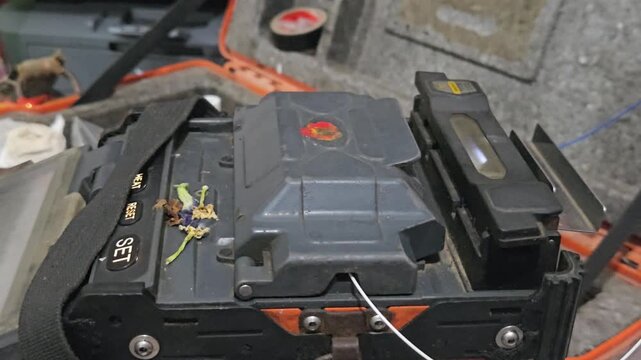 Close-up of a technician performing fiber optic fusion splicing using a precision machine to connect optical cables. The footage highlights high-speed internet infrastructure