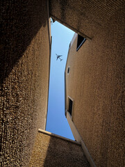 Naklejka premium Plane overhead between textured building walls