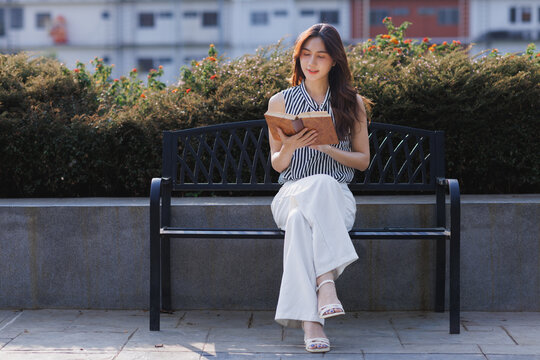 Young asian woman reading book on park bench