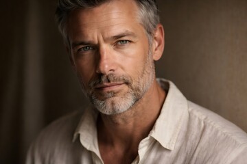 Obraz premium Portrait of a confident, handsome man with graying hair and beard, presenting a thoughtful and experienced expression against a warm, neutral background