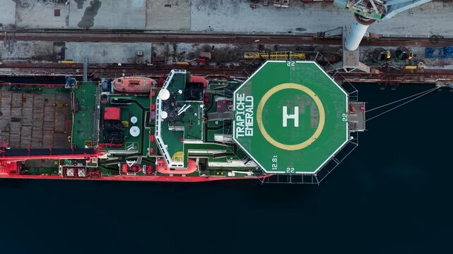 Aerial view of the helipad ship docked in port, juxtaposing the red and green hues against the dark blue water, Pula, Istria County, Croatia.
